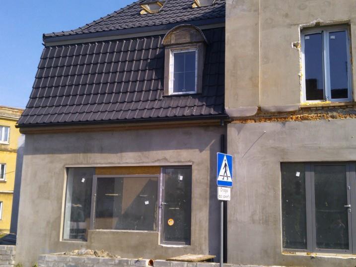 Budynek w trakcie remontu: nowa, ciemna dachówka, okno w lukarnie, surowa elewacja z oknami i drzwiami. Znak drogowy 'Przejście dla pieszych'.