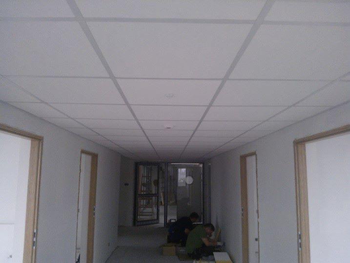 Montaż sufitu podwieszanego kasetonowego w korytarzu biurowym, widoczni dwaj pracownicy podczas instalacji. Świeżo pomalowane ściany i ościeżnice.