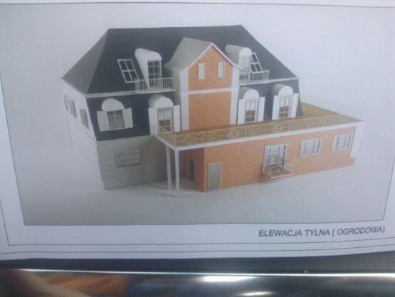 Model architektoniczny dwukondygnacyjnego domu z ciemnym dachem, balkonem i oknami ze szprosami, przedstawiony jako elewacja tylna (ogrodowa).