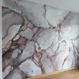 Ściana z dekoracyjną fakturą imitującą marmur w odcieniach szarości, różu i bieli, z żyłkami w kolorze miedzianym, widoczne gniazdko elektryczne.
