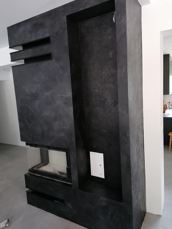 Nowoczesna zabudowa kominkowa w odcieniach szarości z wnęką, wykończona dekoracyjnym tynkiem imitującym beton, z widocznymi poziomymi elementami i drzwiczkami kominka.