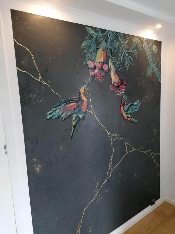 Ściana z ciemną, strukturalną farbą, ozdobiona ręcznie malowanym motywem kolibrów pijących nektar z kwiatów, z delikatnymi złotymi pęknięciami imitującymi żyły minerału.