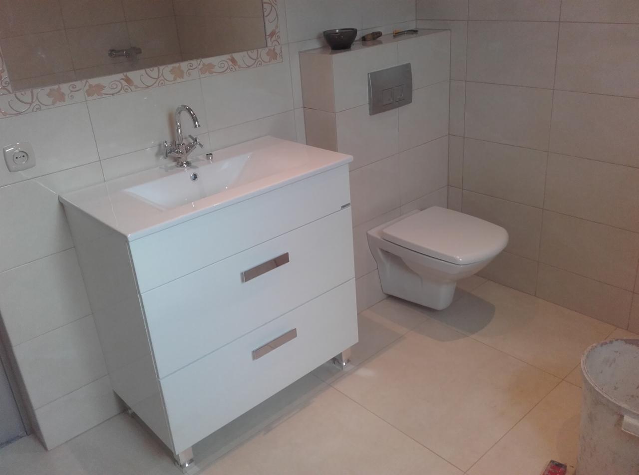 Biała szafka umywalkowa z chromowanym kranem i wisząca toaleta w wykończonej, jasnej łazience. Delikatny wzór na płytkach nadaje wnętrzu subtelny charakter.