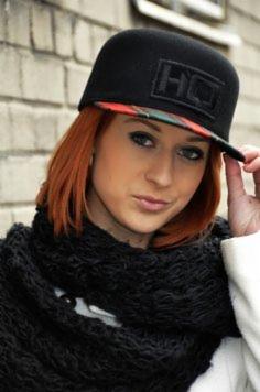 Portret kobiety z rudymi włosami w czarnej czapce z daszkiem Snapback HQ Caps i grubym czarnym szalu na tle ceglanej ściany w Warszawie.