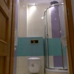 Rembest - Wykończona łazienka z kabiną prysznicową, toaletą podwieszaną i turkusowymi akcentami. Widok zza otwartych, drewnianych drzwi.