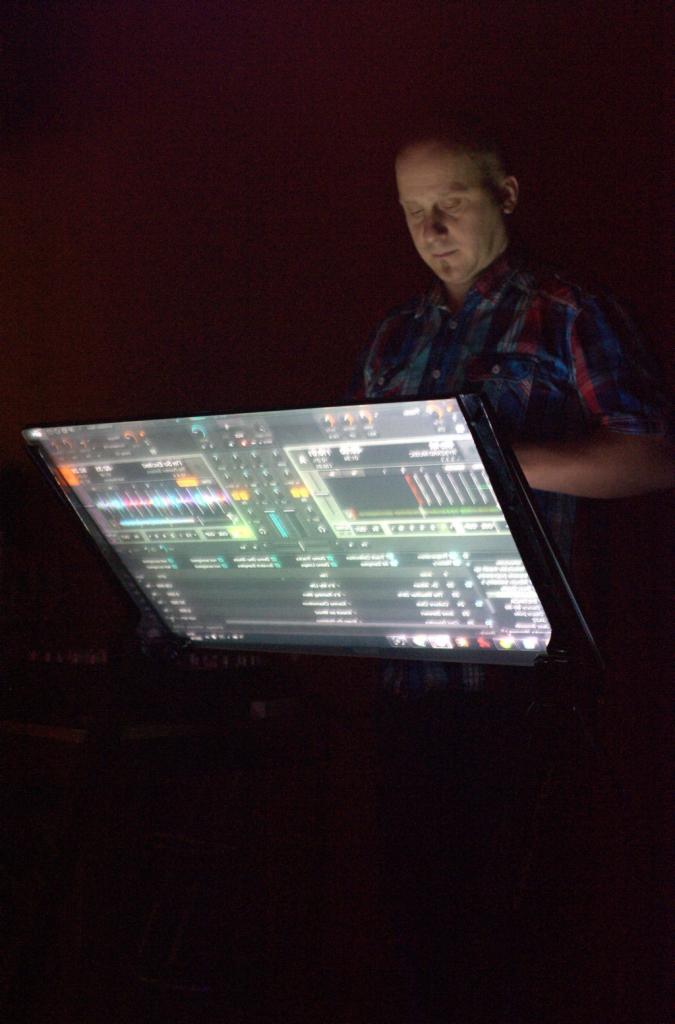 Mężczyzna w koszuli w kratę pracuje na podświetlonym, dotykowym ekranie z oprogramowaniem do miksowania muzyki w ciemnym otoczeniu.