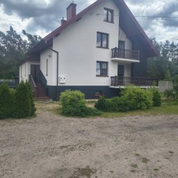 USŁUGI REMONTOWE MARCIN WIECZOREK - Biały dom jednorodzinny z ciemnobrązowym dachem, oknami i dwoma balkonami z rzeźbionymi balustradami. Widoczne zewnętrzne schody, ciemna podmurówka i pochmurne niebo.