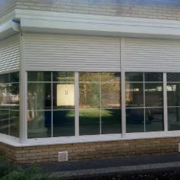 Zewnętrzne, białe rolety opuszczone na oknach oranżerii z cegły, widok z zewnątrz.