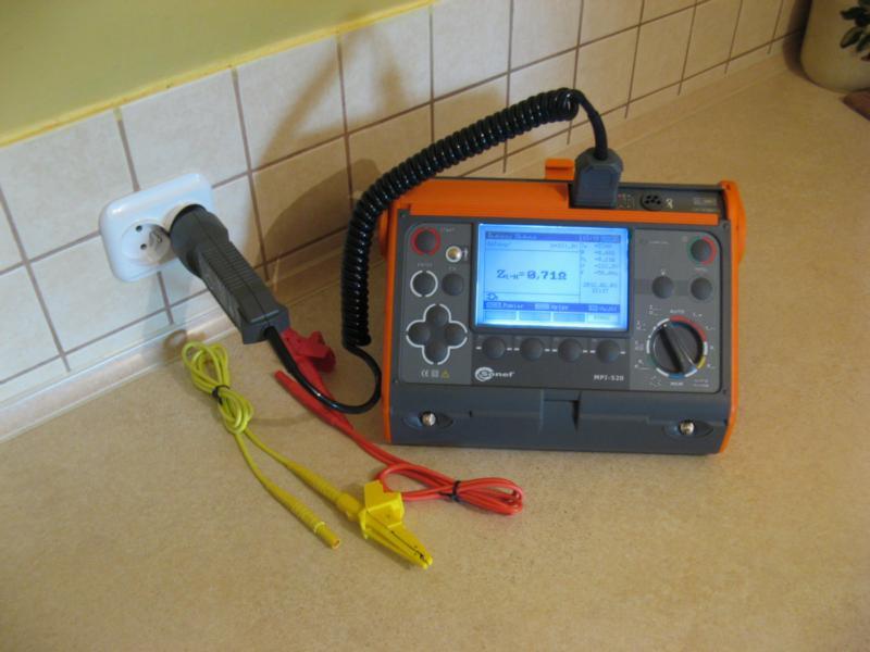 Miernik instalacji elektrycznej Sonel MPI-520 z podłączoną wtyczką do gniazdka, kable pomiarowe z krokodylkami leżą na blacie, widoczny wynik pomiaru impedancji pętli zwarcia na wyświetlaczu.