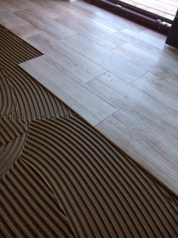 Układanie podłogi z płytek imitujących drewno, widoczna warstwa kleju z charakterystycznymi rowkami i ułożona część podłogi.