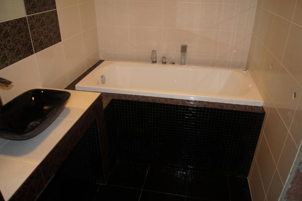 Nowoczesna łazienka z czarną umywalką na blacie i wanną obłożoną czarną mozaiką. Beżowe płytki na ścianach, wzorzysty fragment ściany.