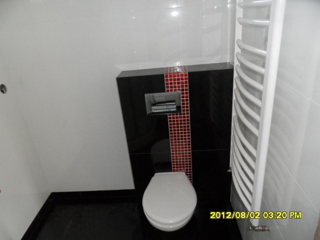 Nowoczesna łazienka z czarno-białymi płytkami, podwieszaną toaletą i grzejnikiem drabinkowym. Czerwony akcent z mozaiki dodaje charakteru.