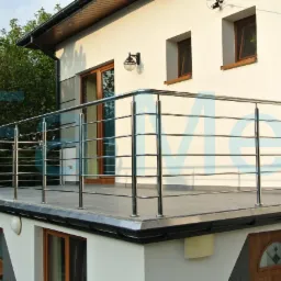 Balkon z nowoczesną, poziomą balustradą ze stali nierdzewnej, z widocznymi detalami mocowań i eleganckim wykończeniem. Tło stanowi biała elewacja budynku.