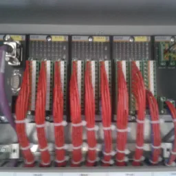 Wnętrze szafy sterowniczej z modułami elektronicznymi i uporządkowanymi wiązkami czerwonych kabli, zabezpieczonych białymi opaskami zaciskowymi.