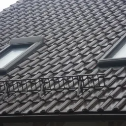 Ciemnobrązowa dachówka ceramiczna z dwoma oknami dachowymi i barierą śniegową, widoczna z bliska.