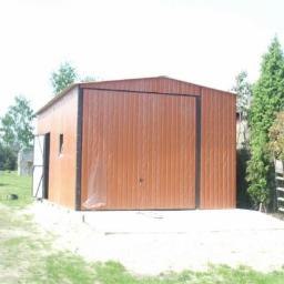 FPHU KAMSTAL Kamil Dyląg - Brązowy garaż blaszany z czarną ramą bramy, ustawiony na betonowej wylewce. Obok drabina oparta o drzewo, na trawniku osoba w niebieskim kombinezonie.