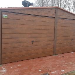 FPHU KAMSTAL Kamil Dyląg - Brązowy garaż dwustanowiskowy z paneli imitujących drewno, z pracownikiem na dachu w trakcie montażu, na czerwonej kostce brukowej, zimowy krajobraz w tle.