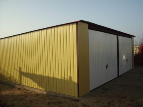 Żółto-biały garaż blaszany z dwoma bramami, widoczny z boku w słoneczny dzień. Konstrukcja z blachy trapezowej, brązowe obramowania.