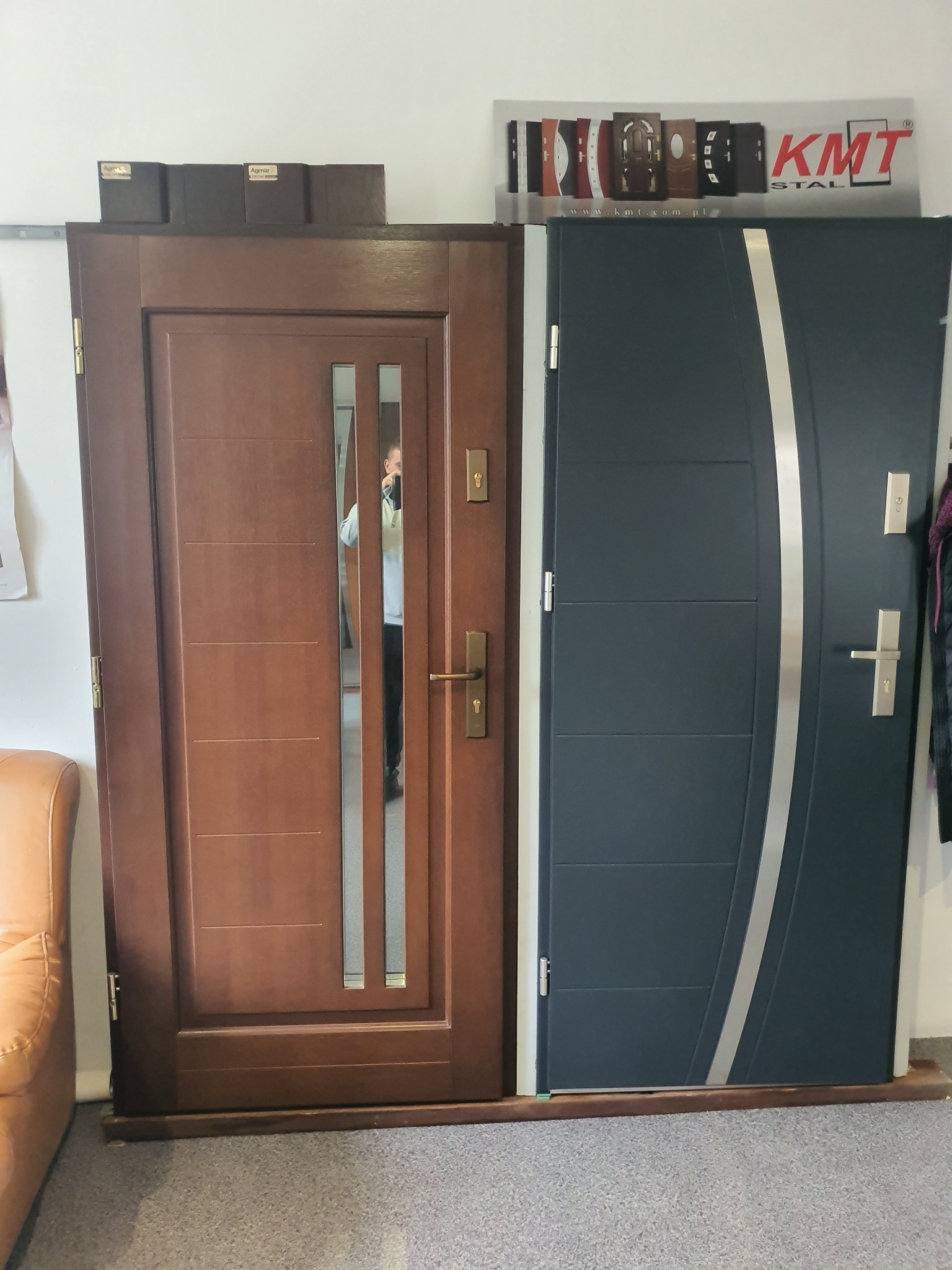 Ekspozycja dwóch modeli drzwi zewnętrznych: brązowe z szybą i grafitowe z srebrnym akcentem, prezentowane w salonie sprzedaży.