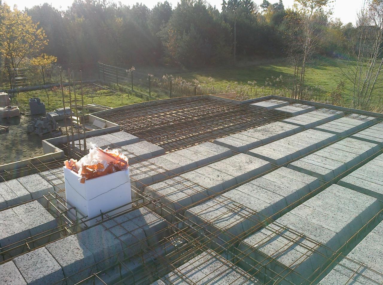 Budowa stropu Teriva z pustaków betonowych i zbrojenia, widok z góry na plac budowy w słoneczny dzień. Elementy szalunkowe i materiały izolacyjne na pierwszym planie.