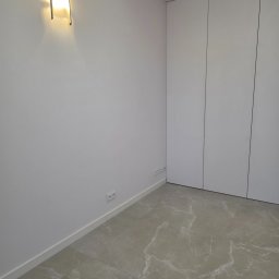 PROCOMPLEX INTERIOR SP.Z O.O. - Minimalistyczne wnętrze: gładkie, białe ściany, marmurowe płytki podłogowe i wbudowana szafa z frontami bez uchwytów. Oświetlenie ścienne dodaje ciepła.