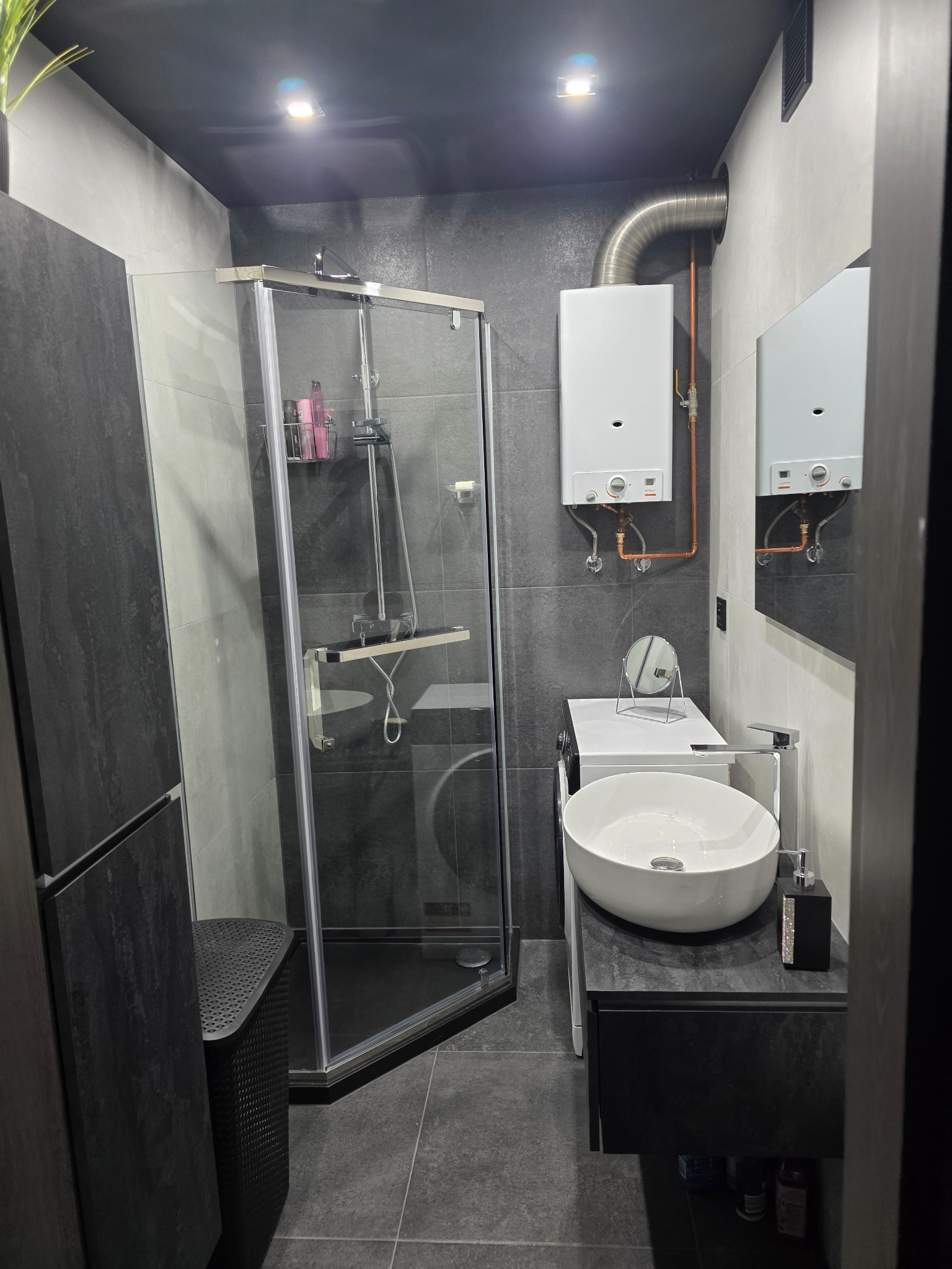 Nowoczesna łazienka w szarościach: kabina prysznicowa, umywalka nablatowa i piec gazowy. Minimalistyczny design z akcentami srebra i czerni.