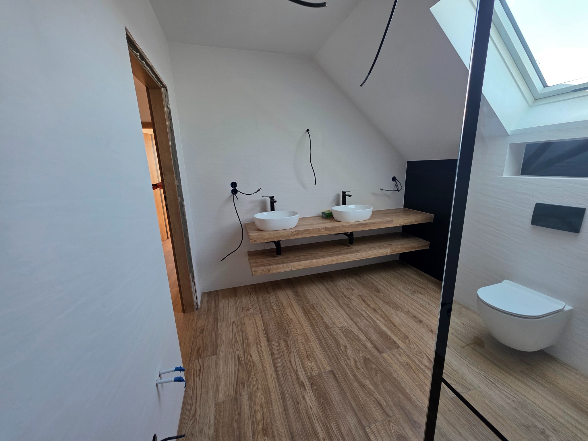 Nowoczesna łazienka na poddaszu z drewnianą podłogą, umywalkami na drewnianym blacie i podwieszaną toaletą. Widoczne elementy instalacji. Ukończony remont.