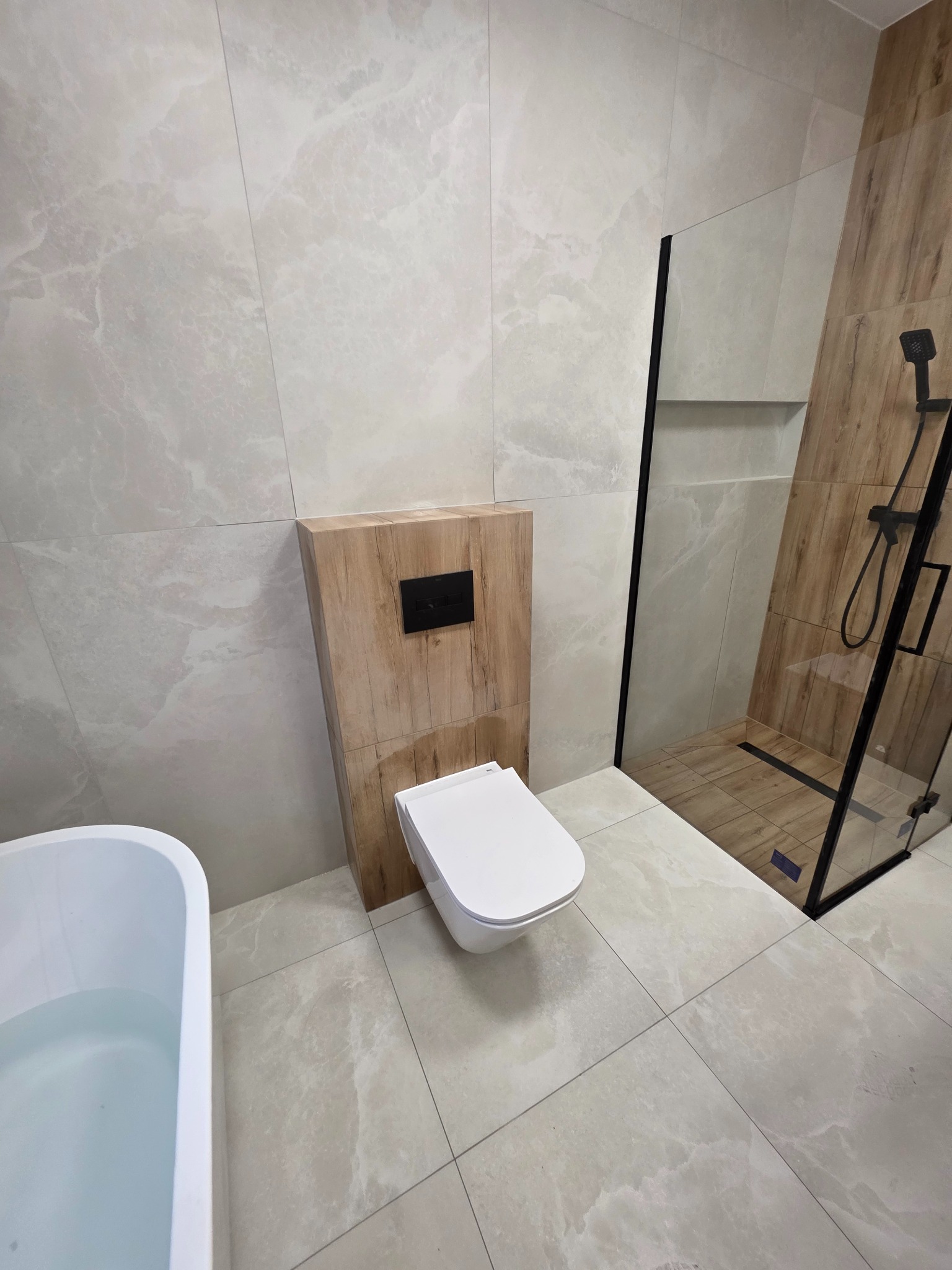 Nowoczesna łazienka z beżowymi płytkami imitującymi marmur, podwieszana toaleta z drewnianą obudową i kabina prysznicowa typu walk-in z czarnymi elementami.
