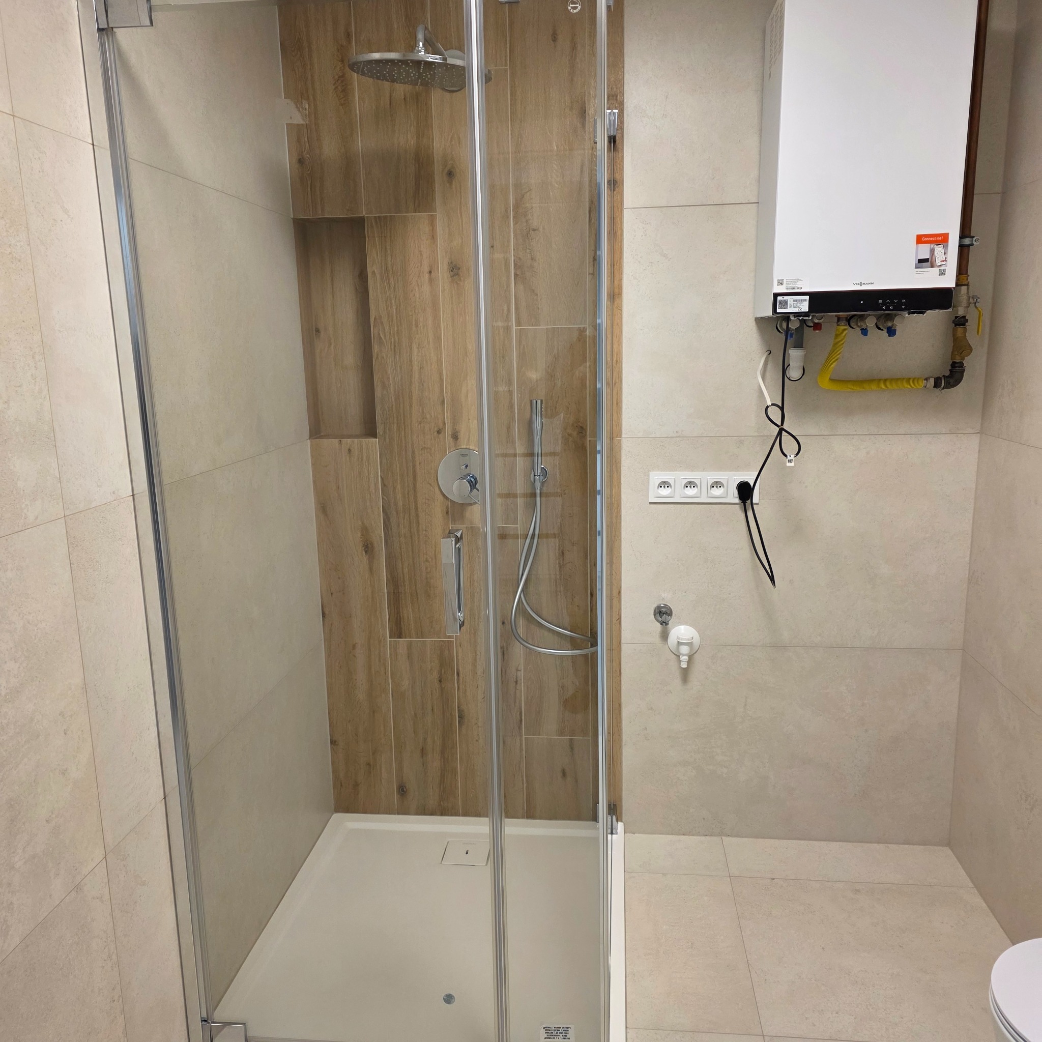 Nowoczesna kabina prysznicowa z deszczownicą i drewnopodobnymi płytkami w beżowej łazience z zamontowanym piecem gazowym.