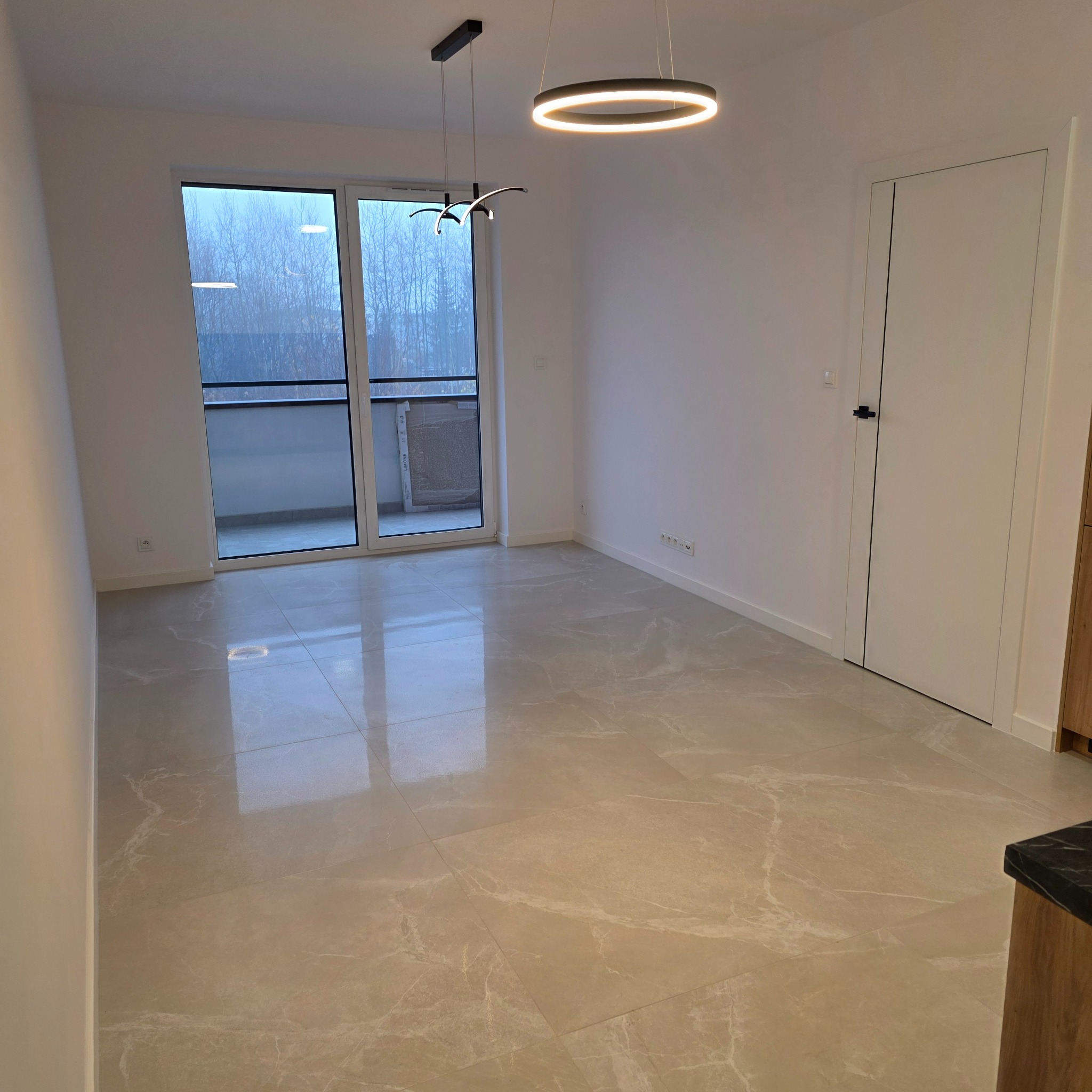 Jasne, marmurowe płytki podłogowe w nowym, pustym pokoju z balkonem i nowoczesnym oświetleniem. Widoczne gniazdka elektryczne i drzwi.