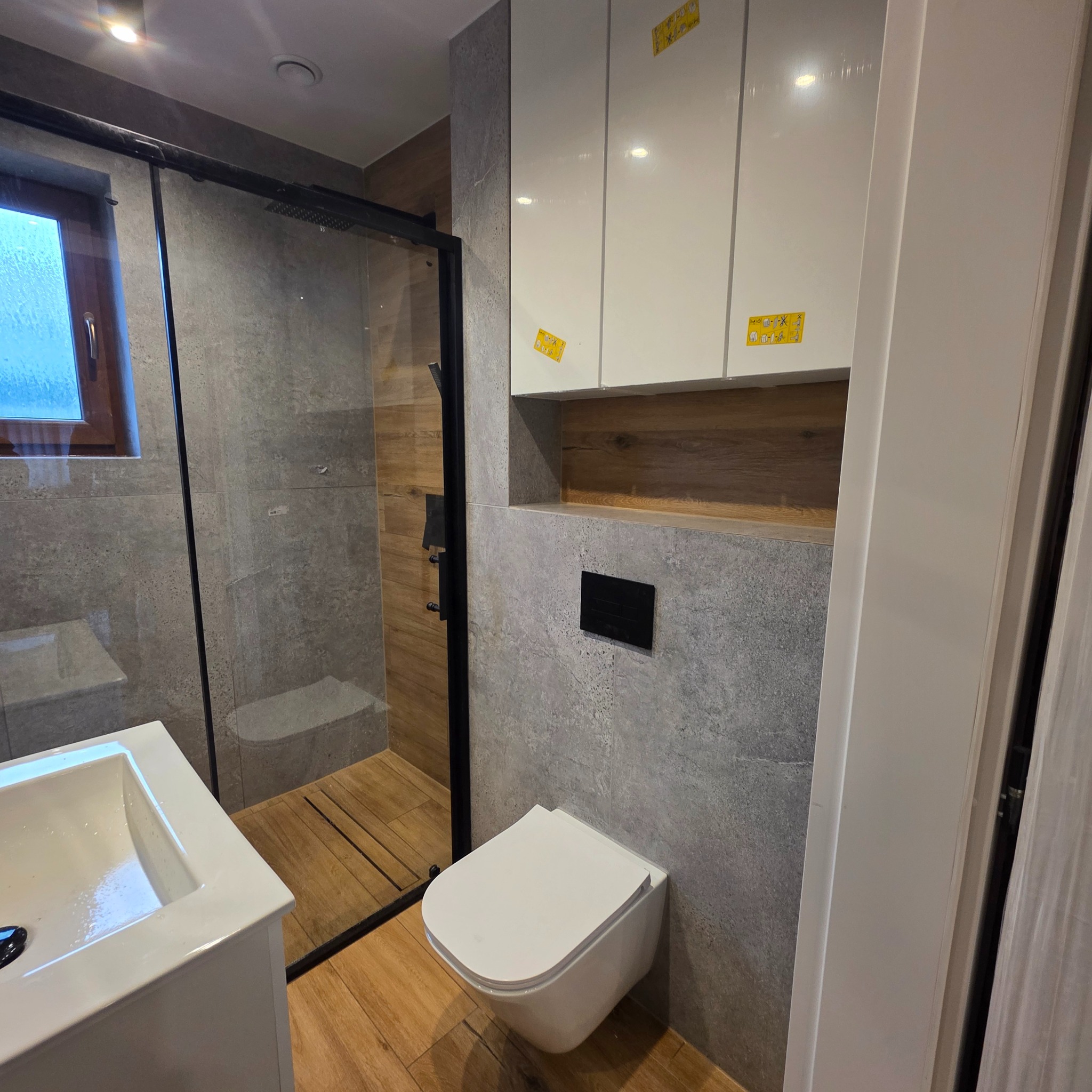Nowoczesna łazienka z kabiną typu walk-in, umywalką nablatową i podwieszaną toaletą. Szare płytki imitujące kamień i drewnopodobne akcenty tworzą spójną całość.