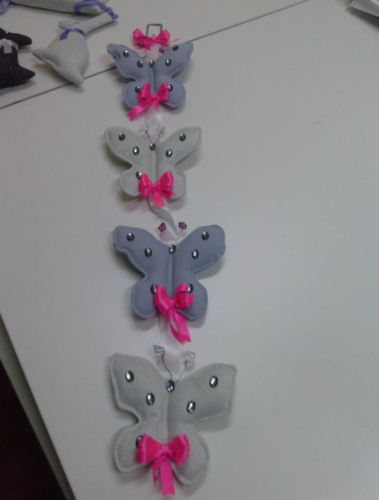 Dekoracyjne, ręcznie szyte motyle z filcu w odcieniach szarości i bieli, ozdobione różowymi kokardkami i srebrnymi dżetami, zawieszone na białym tle.
