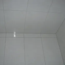 Białe, kwadratowe płytki ceramiczne na ścianie i suficie w rogu łazienki, z widoczną fugą i narożnikiem ściany.