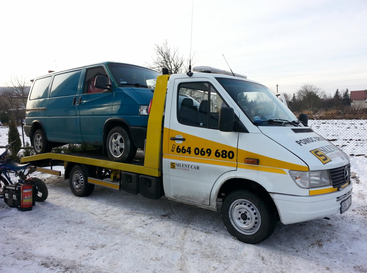 Laweta z niebieskim busem na platformie, widoczny numer telefonu i logo 'Silent Car', zimowy krajobraz w tle, częściowo widoczny motocykl i agregat.