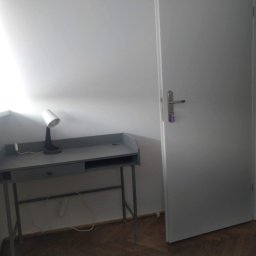 Greg-Bud Usługi Remontowo Budowlane - Świeżo pomalowany pokój z biurkiem i lampką, widoczna biała ściana i drzwi, minimalizm w wystroju.