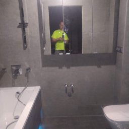 Greg-Bud Usługi Remontowo Budowlane - Nowoczesna łazienka z szarymi płytkami, podświetlaną wanną i lustrem w szafce, w którym odbija się osoba robiąca zdjęcie.