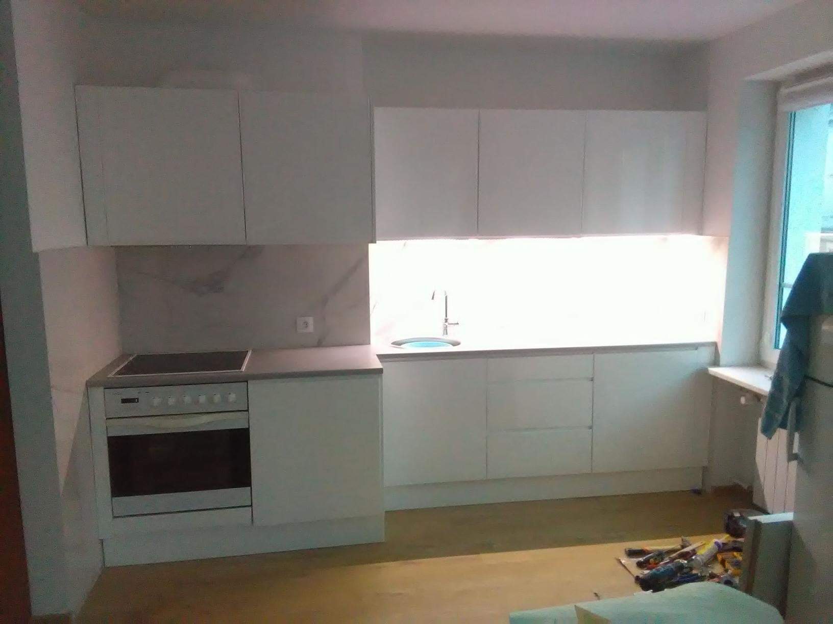 Biała zabudowa kuchenna z płytkami imitującymi marmur nad blatem, widoczne narzędzia na podłodze.