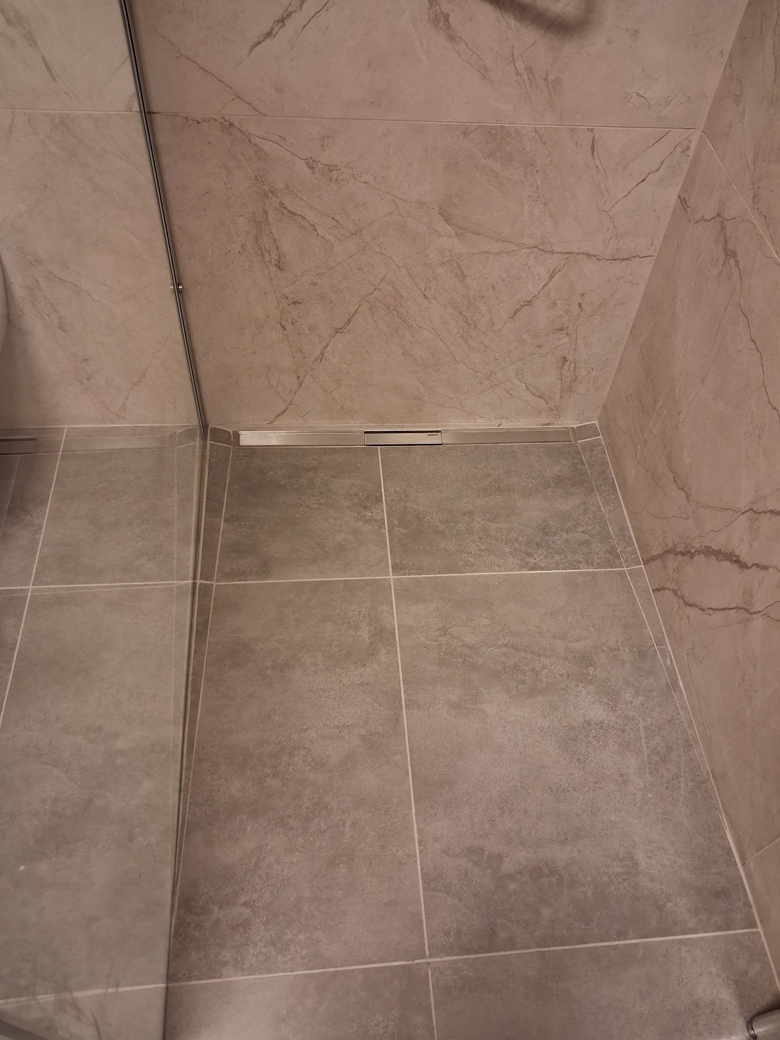 Szare płytki podłogowe w kabinie prysznicowej z odpływem liniowym, marmurowa okładzina ścienna w odcieniach beżu i szarości.