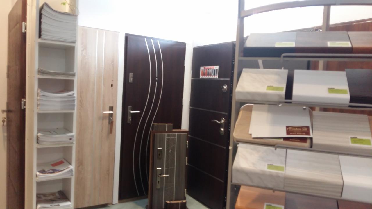 Ekspozycja różnych modeli drzwi zewnętrznych w salonie, z widocznymi próbkami wykończeń i katalogami.