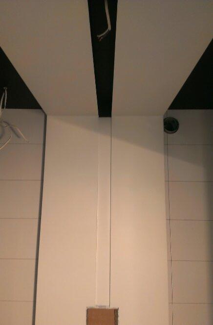 Biały sufit z czarnymi wstawkami i białe ściany z poziomymi panelami, widok z dołu, w trakcie wykańczania wnętrza.