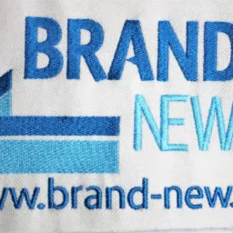 Biała tkanina z niebieskim haftem logo 'BRAND NEW' i adresem strony www.brand-new.pl. Precyzyjne wykonanie w Łodzi.