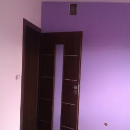 Ciemne, drewniane drzwi z przeszkleniem w otwartym ościeżu, na tle fioletowej i r&oacute;żowej ściany. Widoczne fragmenty podłogi z paneli.