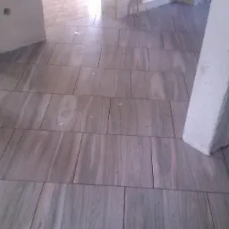 Ułożone płytki podłogowe imitujące drewno w jasnym pomieszczeniu. Widoczny fragment grzejnika i surowego słupa. Ujęcie z niskiego kąta.