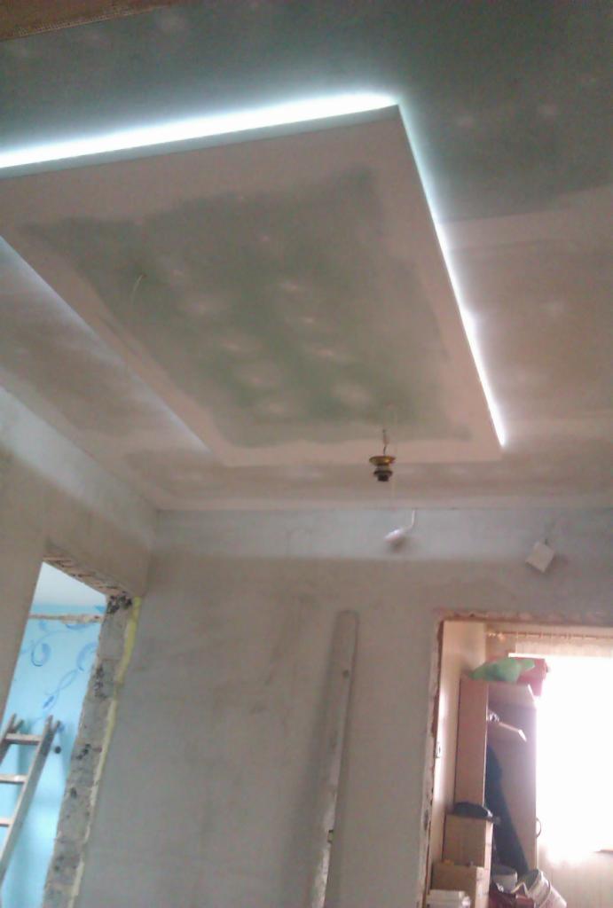 Podwieszany sufit z oświetleniem LED w trakcie wykańczania, widoczne ślady szpachlowania, surowy stan ścian, wnętrze w trakcie remontu.