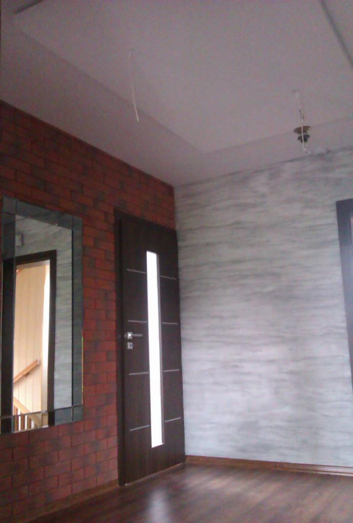 Wnętrze po remoncie: ciemne panele, ściana z efektem cegły i lustro, drzwi z przeszkleniem, ściana z efektem malowania, sufit z wystającym kablem.