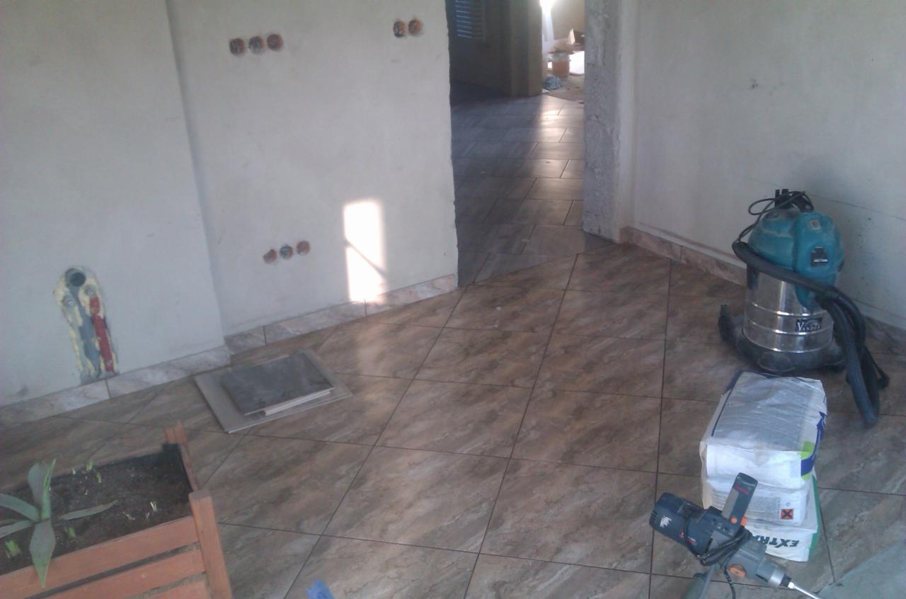 Ułożone brązowe płytki podłogowe w nowym wnętrzu. Widoczne przygotowane ściany, odkurzacz przemysłowy i mieszadło do zaprawy.