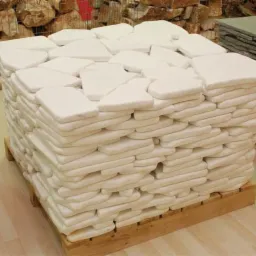 Paleta z ułożonymi warstwami nieregularnych, białych płyt kamiennych, gotowych do transportu, z paletą szarych płyt w tle.