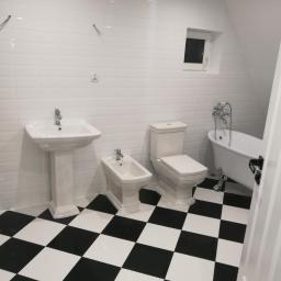 Arkadiusz Piorkowski - Wykończona łazienka w stylu retro z białą armaturą, czarno-białą szachownicą na podłodze i białymi płytkami na ścianach, oświetlona punktowo.