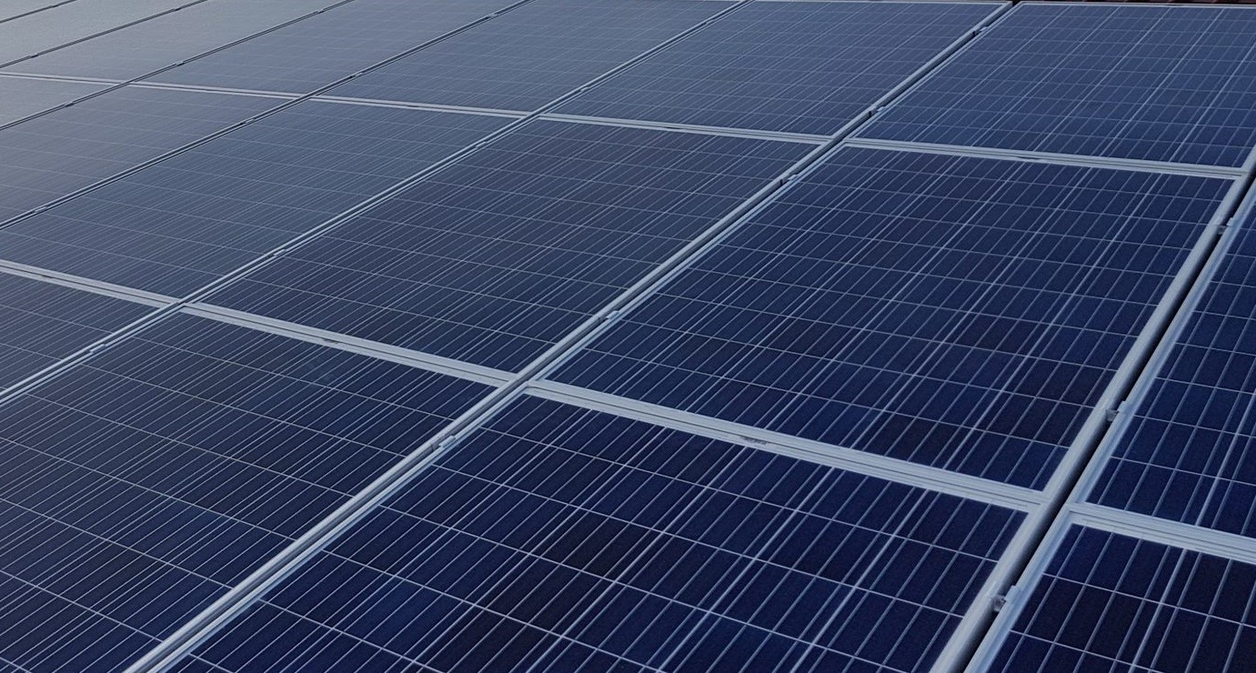 Równomiernie ułożone panele słoneczne w kolorze ciemnoniebieskim z widocznymi srebrnymi ramami i mocowaniami, tworzące regularną siatkę na dachu.