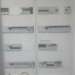 Rozdzielnica elektryczna z zamontowanymi bezpiecznikami i wyłącznikami różnicowoprądowymi marki Eaton, widoczne kable oraz oznaczenia sekcji i numerów poszczególnych elementów.